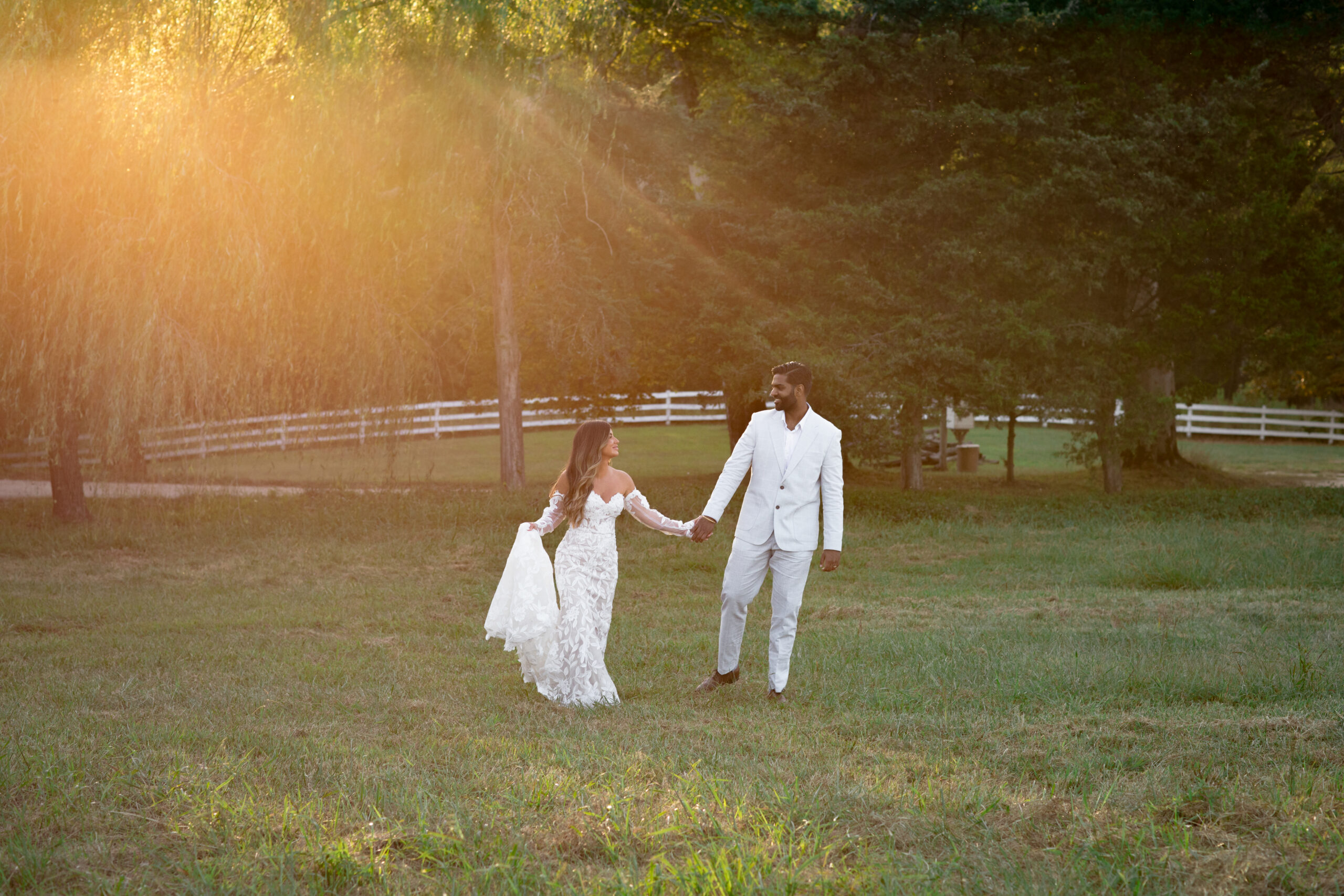 Newly wed couple holding hands at sunset in beautiful field.